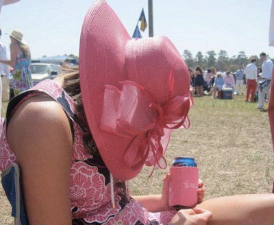 A young adult woman wearing a pink sun hat and a sundress slumped over a chair holding (presumably) a beer.