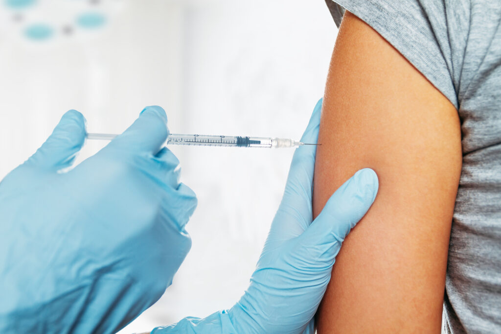 A nurse's hand injecting a syringe with clear liquid into a woman's arm.