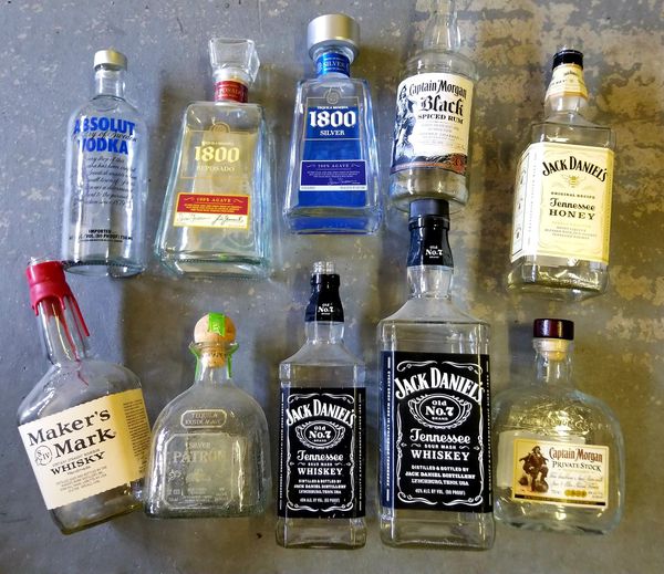 A picture of 10 different liquor bottles laid on the ground, all empty.