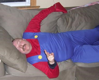 A man passed out on a tan couch wearing a Mario costume.