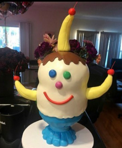 A weird ice cream sundae that looks like an animated character -- M&Ms for eyes and nose, licorice for a mouth, and bananas with raspberries for arms and an extra banana sprouting out of the top of its head.