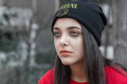 An image of a dark haired teenage girl in a black Nirvana cap and a red shirt with mascara lines from recent crying running down her cheeks.