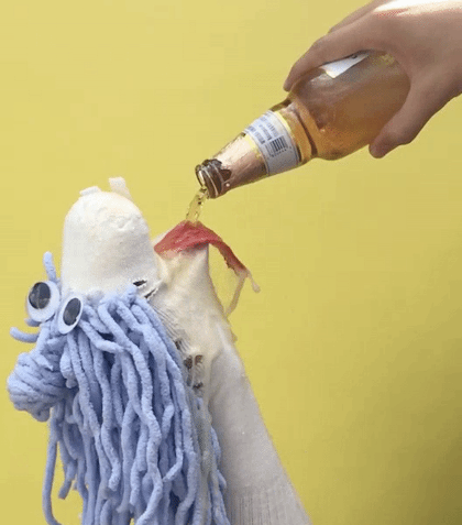 A picture of someone pouring a bottle of beer into a sock puppet.
