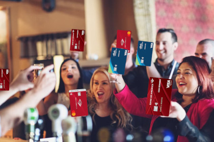 A group of people at a party holding up drinks for a toast, except all of the drinks have been replaced with various Bank of America credit cards