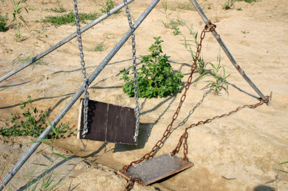 A broken swing set, which has largely fallen down, rusted, and is in major disrepair.