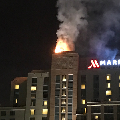 A picture showing a fire bellowing out of the top of a tower on a Marriott hotel