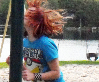 A picture of a woman with red hair and a blue shirt walking into a pole at a playground.