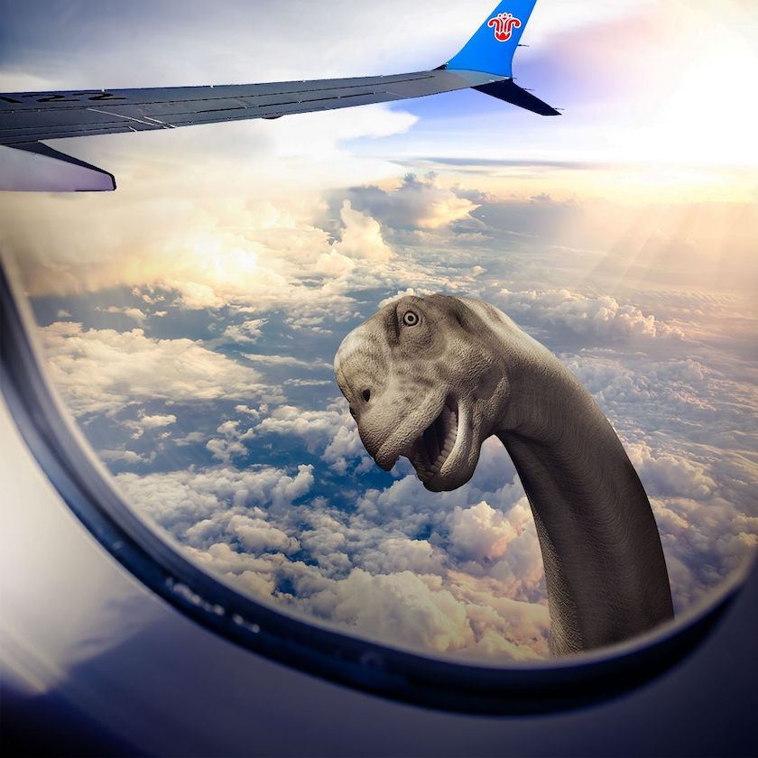 A picture looking out of an A330 aircraft window at altitude, with a brontosaurus peeking in.